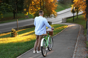 Fototapeta premium Happy man walking his bicycle in park on sunny day, back view