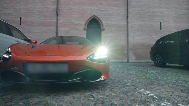Sleek orange sports car parked on the street with switched on headlights against background of red brick building, exclusive collection of expensive automobiles with shiny design, sports cars racing