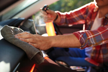 Man wiping car dashboard with grey microfiber rag in salon, closeup