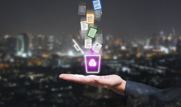 Hand holding glowing hologram recycle bin with digital documents falling, symbolizing file deletion, secure data management, cloud technology, and modern cybersecurity concept.