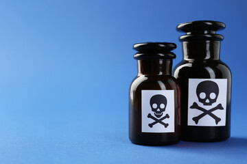 Bottles of poison with warning signs on light blue background, closeup. Space for text