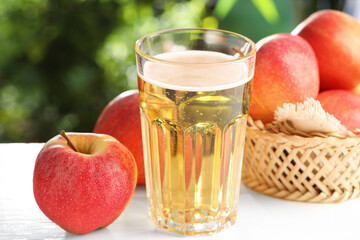 Delicious cider in glass and apples on white wooden table outdoors, closeup