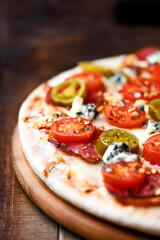 Pizza with salami, jalapeno pepper, cherry tomatoes and mozzarella cheese. Soft focus.	