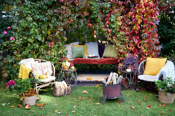 Cozy autumn terrace with rustic decor, wicker chairs, colorful pillows, firewood basket, and seasonal pumpkins. Decorative plants and vibrant fall foliage create a warm, inviting outdoor retreat, perf