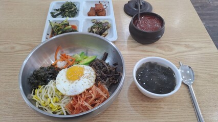korean bibimbap rice bowl with side dishes and gochujang on a wooden table