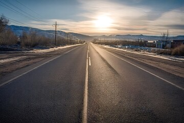 Empty asphalt highway stretching into the distance towards a golden sunset over mountains, conveying themes of travel, journey, freedom, and future exploration during an evening drive