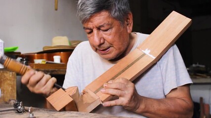 A Colombian luthier polishes a piece of wood with a tool to make a typical acoustic guitar in a workshop in Neiva, Huila, Colombia. Concept of handmade - Powered by Adobe
