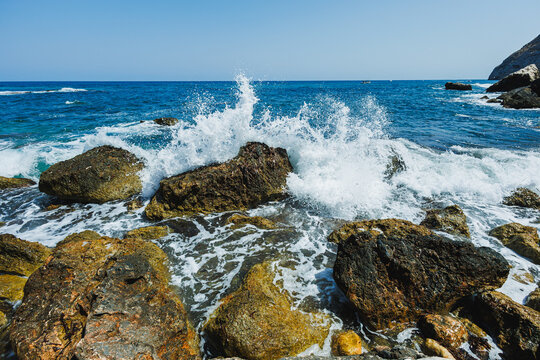 Waves crash against rocky shore on a bright sunny day, showcasing nature's power in a serene coastal setting - Powered by Adobe