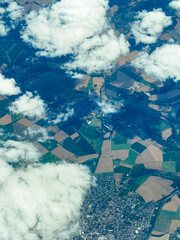 Bird's eye view of patchwork fields and clouds over a quaint town in the early afternoon with merging shades of green and brown creating a beautiful landscape