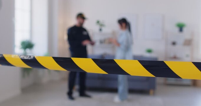 Closeup shot of an yellow police tape marking a crime scene at a home. A policeman and a witness provide testimony and gather evidence related to a homicide or accident investigation.
