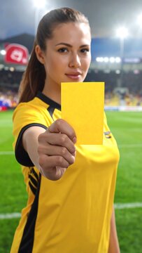 Confident female football referee showing a yellow card as a disciplinary warning during a match in a professional stadium