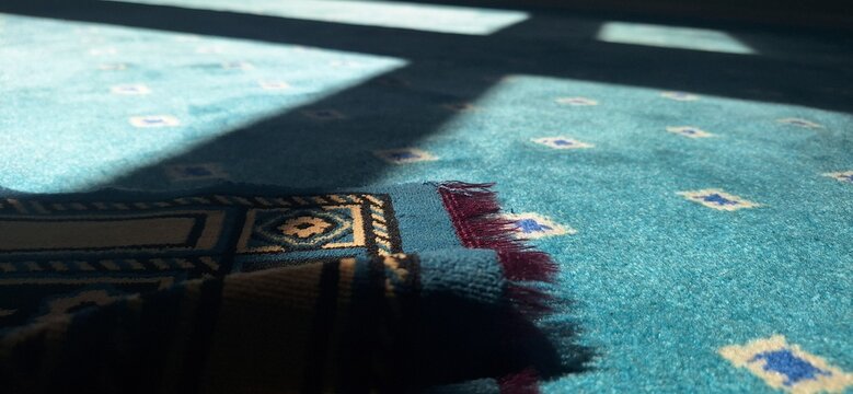 A blue prayer mat is placed on a patterned blue carpet in a daytime setting
