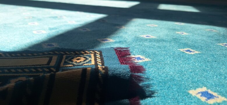 A blue prayer mat is placed on a patterned blue carpet in a daytime setting