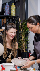 In an art studio two beautiful middle-aged artist friends are working on clay shaping at a table