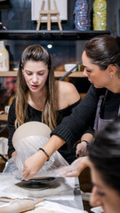 In an art studio two beautiful middle-aged artist friends are working on clay shaping at a table