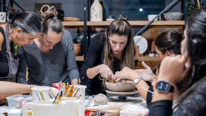 In an art studio during a group art event, a group of women and children are enjoying a creative hobby, learning and having fun as they make shapes out of clay