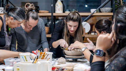 In an art studio during a group art event, a group of women and children are enjoying a creative hobby, learning and having fun as they make shapes out of clay