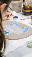 During an art event in a studio, a girl child is painting Christmas ornament shapes she crafted on clay
