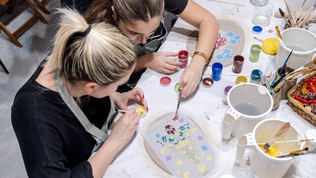 In an art studio during an event, a mother and her young daughter are enjoying quality time together while learning clay shaping as a hobby