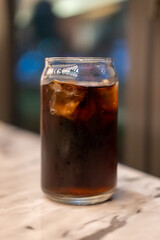 A can shaped glass of Cola on the table with bokeh background