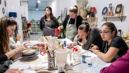 In an art studio during a group art event, a group of women and children are enjoying a creative hobby, learning and having fun as they make shapes out of clay