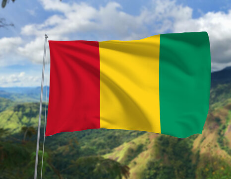 National flag of Guinea waving in the wind against scenic mountain landscape and cloudy blue sky, symbol of patriotism and independence