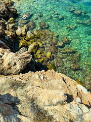 Clear turquoise water gently laps against rocky shore at a tranquil coastal location under bright sunlight