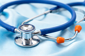 Blue stethoscope with orange earpieces resting on a light blue fabric surface