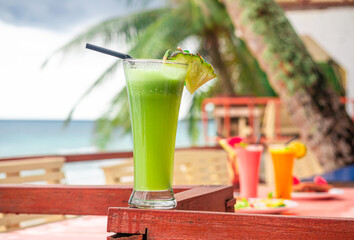 Refreshing tropical green drink with a pineapple garnish on a wooden table by the ocean, perfect for a relaxing beach vacation