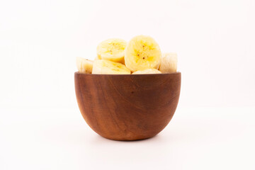 Ripe banana pieces are stacked neatly inside a small brown wooden bowl for healthy breakfast meal.