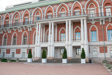 Tsaritsyno showcases its impressive brick building with intricate arches and tall columns, surrounded by neatly trimmed greenery in the courtyard.