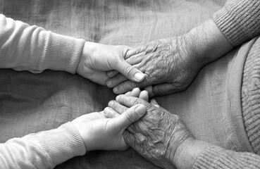 hands touch the hand of an elderly woman. The concept of home care. An elderly woman holds the hand of a young nurse in a nursing home.The concept of elderly care and death