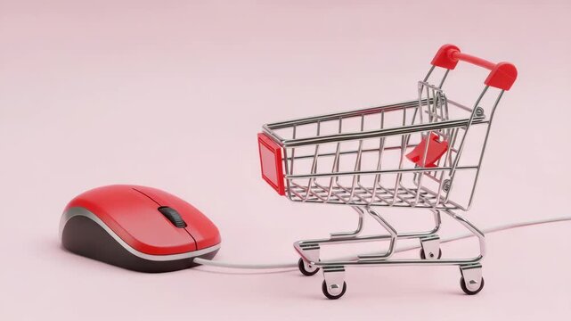 Red computer mouse next to a miniature shopping cart on a pink colored surface studio shot