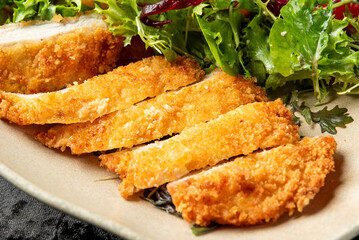 Close-up of crispy breaded chicken cutlets sliced into strips, served with fresh green salad. Golden texture, juicy interior, vibrant presentation. Horizontal, appetizing food shot.