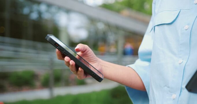 Close-up of a woman s hand swiping on a smartphone outdoors, using the screen to browse or text, showing everyday use of mobile technology and digital communication