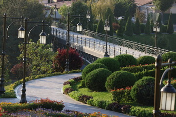 Pathway through a beautifully landscaped park with elegant lampposts and a bridge in the background.