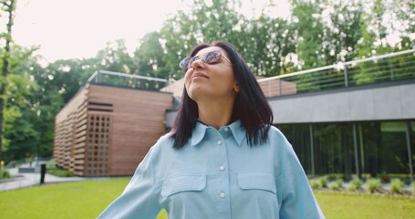 Satisfied young woman enjoys the fresh air while taking a leisurely walk in a green park. She looks relaxed and happy, surrounded by nature on a bright sunny day