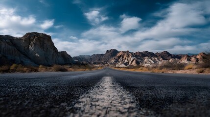 Empty asphalt road leading through a vast desert landscape towards distant mountains under a cloudy blue sky