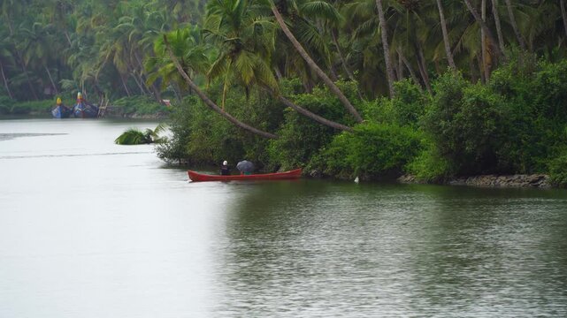 Fishermen on red boat with an umbrella fishing in a rain shower under the coconut trees showing the daily life in Kerala, Tamil Nadu, Karnataka south India