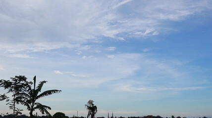 Fototapeta premium Vast blue sky with a mix of soft, wispy white clouds and a clear contrail, creating a beautiful natural backdrop. Distant birds add a sense of scale and life to the open atmosphere.