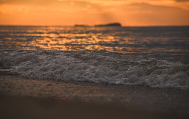 Golden morning light reflecting on ripples along sandy beach.