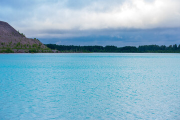 Beautiful aqua blue lake surrounded by forest and hills under a dramatic sky. Tranquil natural scenery with turquoise water and woodland