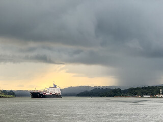 landscape view of area around Panama Canal near Gamboa settlement, almost half way between Pacific Ocean and Caribbean Sea, with a big cargo ship passing the Canal from north to south - dark clouds 
