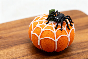 A small orange pumpkin decorated with white icing web and a black plastic spider on a wooden surface