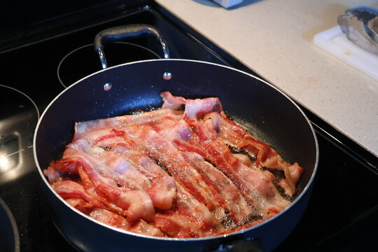 multiple slices juicy bacon sizzling on the frying pan.