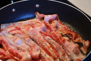 multiple slices juicy bacon sizzling on the frying pan.