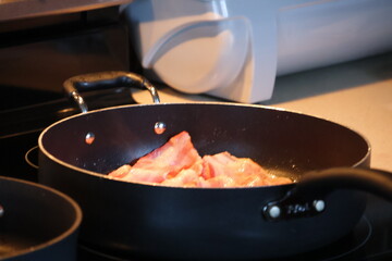 multiple slices juicy bacon sizzling on the frying pan.