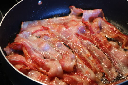 multiple slices juicy bacon sizzling on the frying pan.