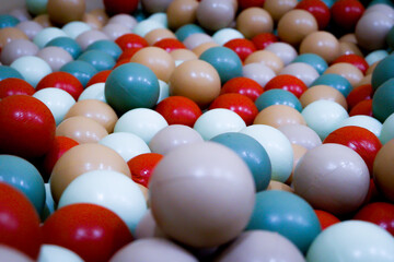 This photo captures a close-up view of colorful plastic balls in a children’s playground ball pit. The balls come in a variety of soft and vibrant colors such as teal, beige, red, white, light brown.