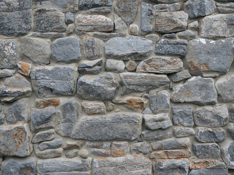 A fieldstone wall made of various rounded grey rocks and mortar. A classic rustic masonry background.